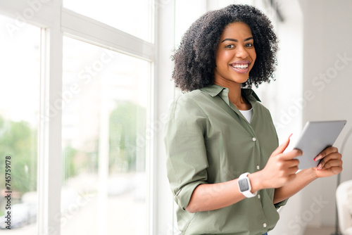 An African-American woman in a relaxed pose, holding a tablet with a confident smile, interacting with friends online or conducting business remotely, highlighting the flexibility of digital devices. photo