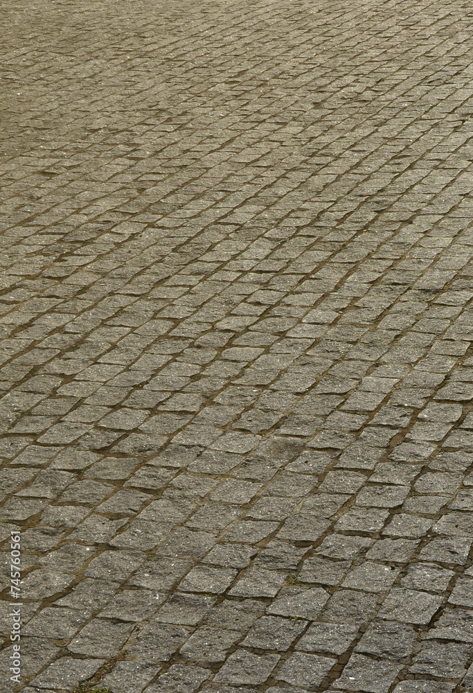 The texture of the paving slab (paving stones) of many small stones of a square shape under bright sunlight
