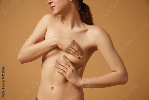 Female health. Cropped image of young woman covering breast with hands in cotton underwear against beige studio background. Concept of body and health care  female beauty  wellness