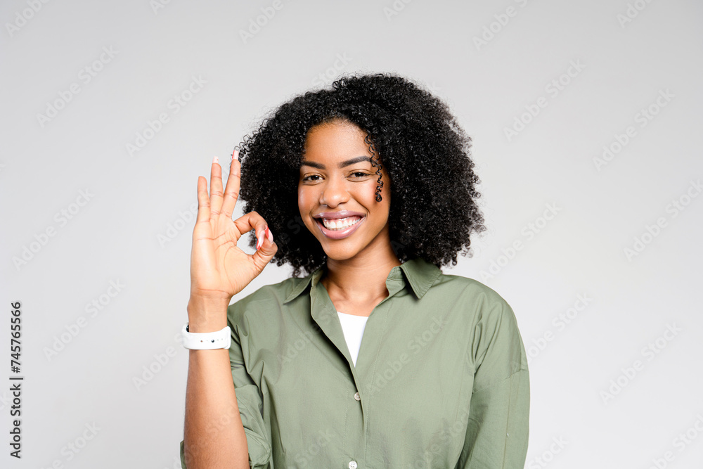 An exuberant African-American woman shows the OK hand gesture, her face alight with a friendly smile. This image perfectly embodies themes of agreement and quality assurance An exuberant African-American woman shows the OK hand gesture, her face alight with a friendly smile. This image perfectly embodies themes of agreement and quality assurance