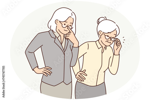 Two elderly women in business clothes carefully look to side watching work of young employees