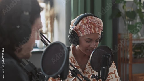 Side closeup of Black woman hosting podcast and talking to unidentified Caucasian man in studio photo