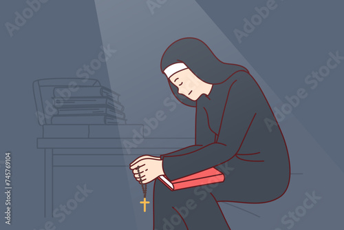 Woman nun sits with head bowed and holds religious crucifix and book of prayers, feeling remorse after committing sin. Catholic female nun located in dark room and praying before going to bed