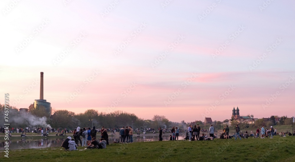 Summer gatherings of students and young people at the bank of Warta river in Poznań for chill, leisure, drinking, making grill. Evening cityscape in the background. Poznan, Poland