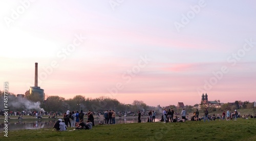 Summer gatherings of students and young people at the bank of Warta river in Poznań for chill, leisure, drinking, making grill. Evening cityscape in the background. Poznan, Poland
