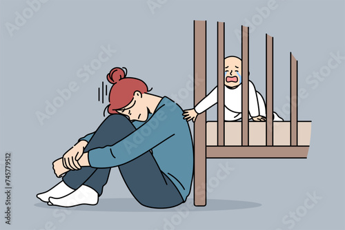 Exhausted mother with postpartum stress sits on floor near crib with crying newborn, and needs help of professional nanny. Postpartum stress in girl who does not pay attention to son