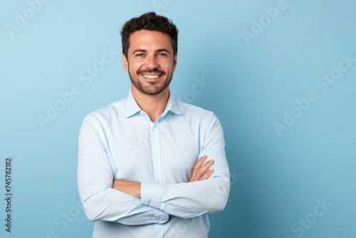 Portrait of a handsome young man standing with arms crossed over blue background © Iigo