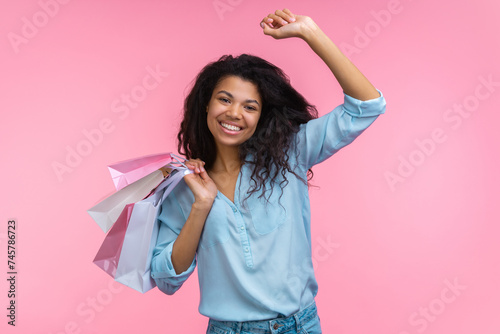 Portrait of happy smiling beautiful cheerful young woman with a bunch of paper bags in hand having fun enjoying shopping, isolated over pastel pink background