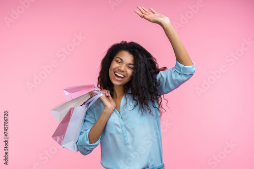 Studio shot of happy smiling beautiful cheerful girl with a bunch of paper bags in hands having fun enjoying shopping, isolated over pastel pink background