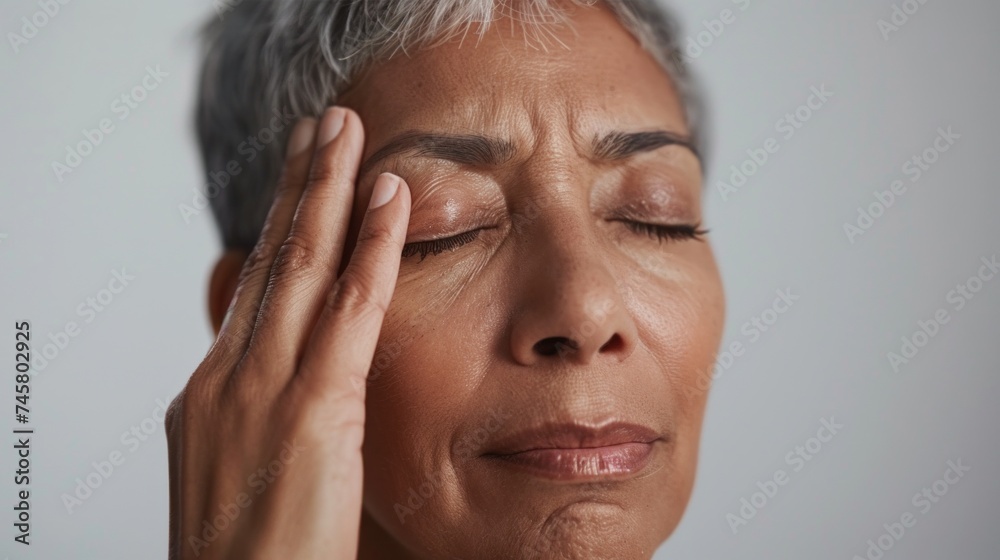 Fototapeta premium A woman with closed eyes pressing her temples with her fingertips possibly indicating stress or deep thought.