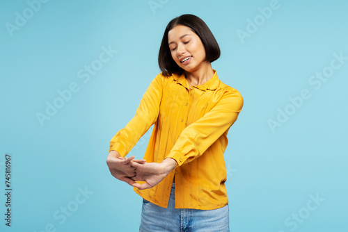 Portrait of smiling attractive Asian woman wearing casual yellow shirt, stretching arms, eyes closed
