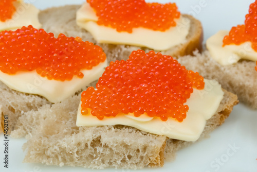 New Year's snack. on a white plate there are small sandwiches with pieces of butter and bright red caviar, close-up, snack concept