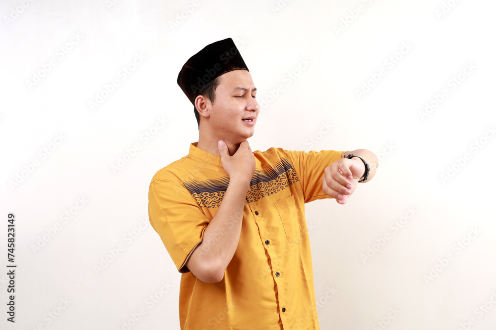 Young asian muslim man feeling thirsty, touching his neck and looking at his wrist watch. Fast month concept Young asian muslim man feeling thirsty, touching his neck and looking at his wrist watch. Fast month concept