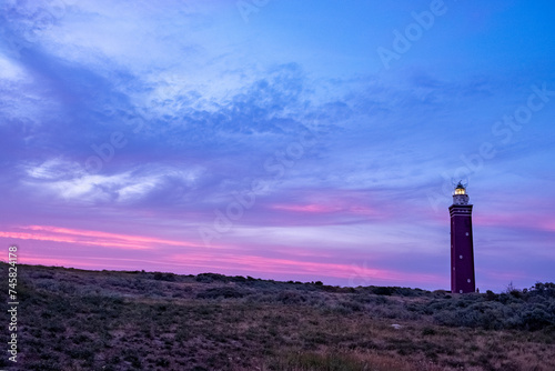 This striking image showcases the silhouette of a lighthouse set against a dramatic sunset sky painted in vivid shades of purple and pink. The lighthouse's beacon shines brightly, a symbol of guidance