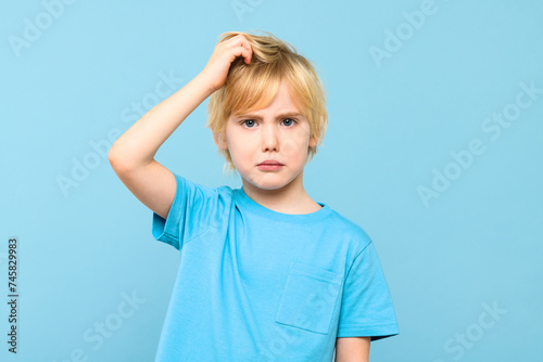 Young doubtful confused boy thinking, scratching head, trying to find solution, isolated on pastel blue background.