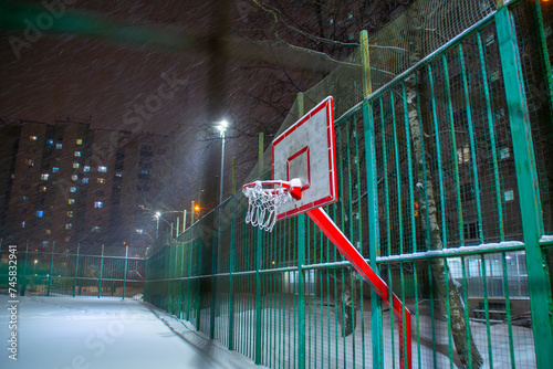 Public basketball court in winter. Close-up of a basketball hoop under the snow.