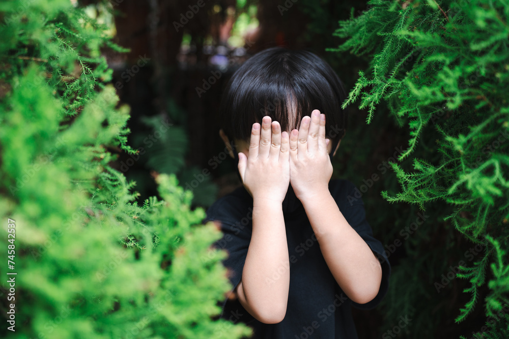 Kids is covering his face with both palms when playing hide and seek game.