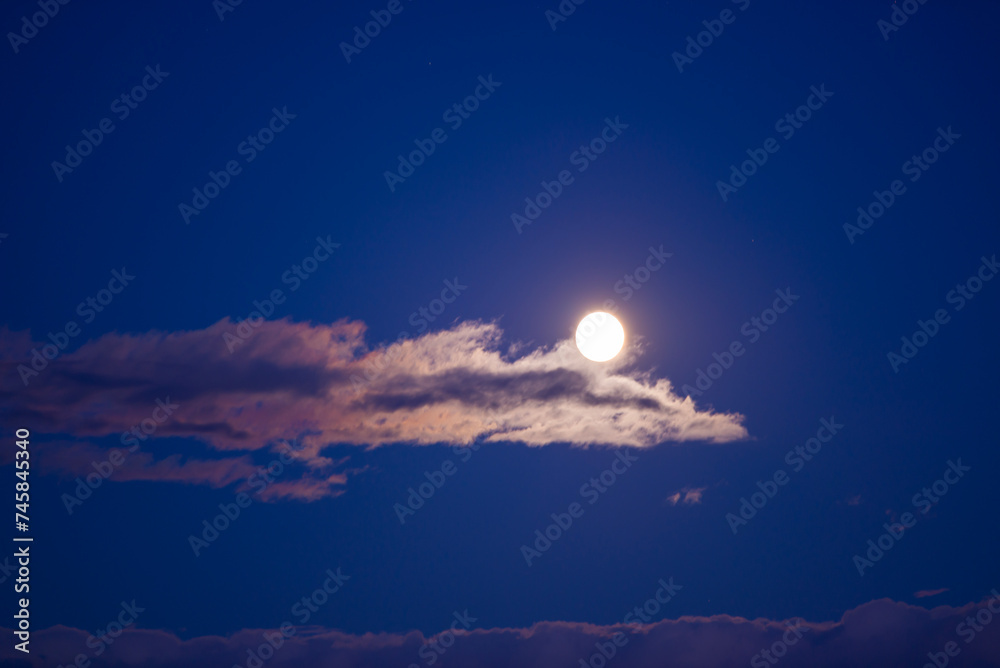 Full moon rising on the sky seen trough brightly clouds during summer season at dusk Full moon rising on the sky seen trough brightly clouds during summer season at dusk