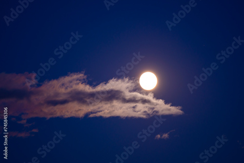 Full moon rising on the sky seen trough brightly clouds during summer season at dusk
