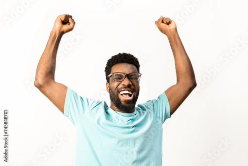 African American man with glasses celebrating a victory, arms raised in excitement, isolated on a white background, conveying happiness and positive emotions.
