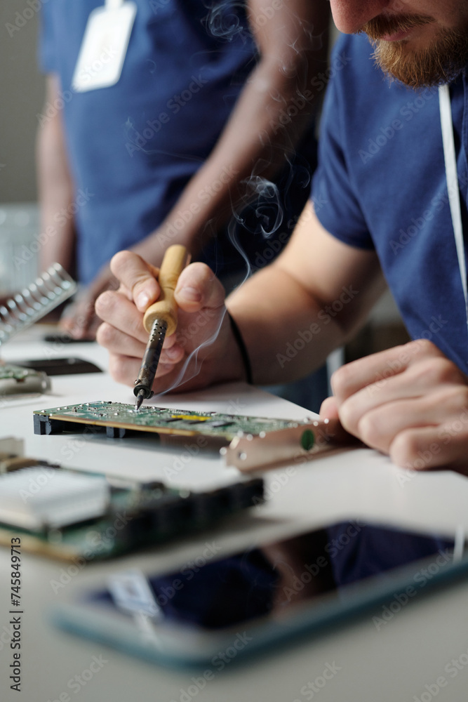 Close-up of young technician of maintenance service using electric handtool while repairing part of computer processor by workplace