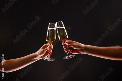 Картината върху платно Two people clinking glasses of sparkling champagne or prosecco against a dark black background, with only their hands and the glasses visible