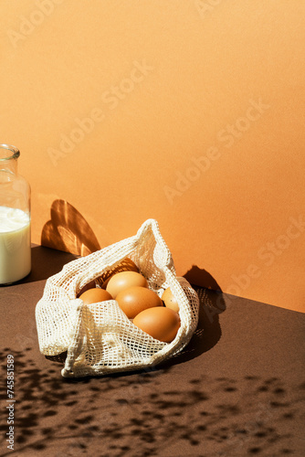 Eggs in a mesh bag with mil in glass bottle on brown backgrouund. Sun light effect with floral shadows. photo