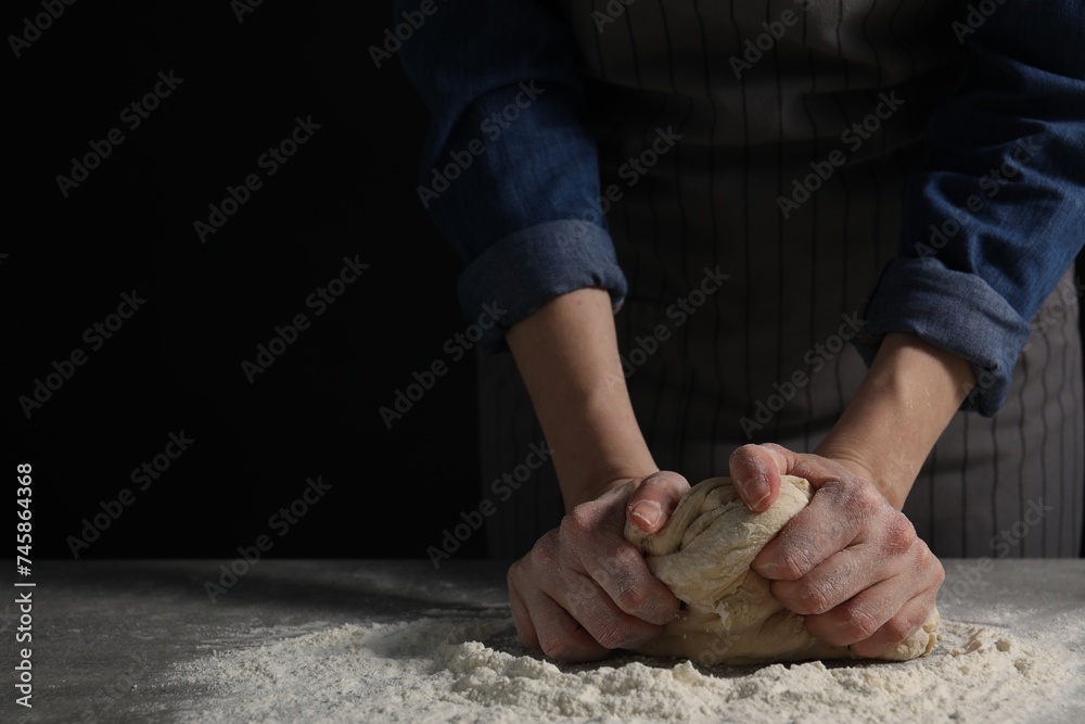 Making bread. Woman kneading dough at table on dark background, closeup. Space for text