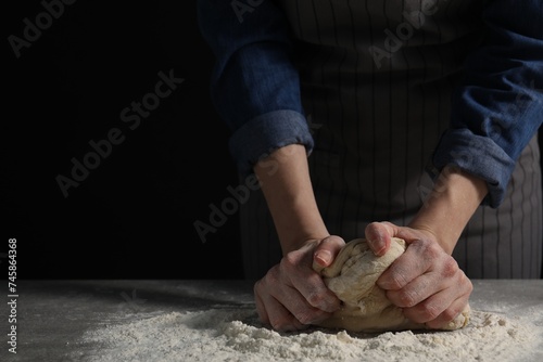Making bread. Woman kneading dough at table on dark background, closeup. Space for text
