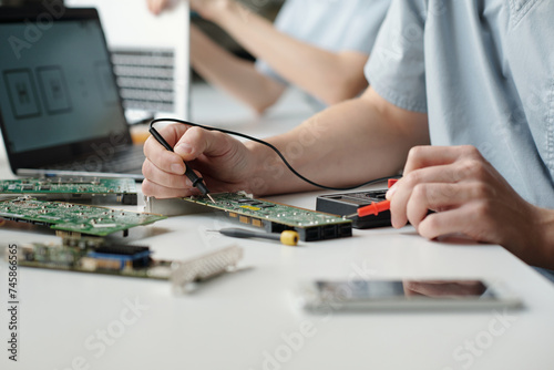Hands of young worker of troubleshooting service center using electric handtool while checking and repairing computer motherboard