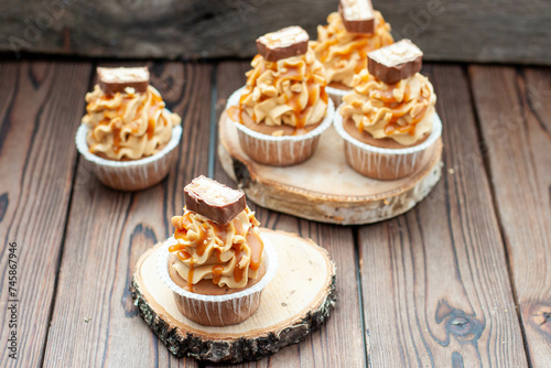 Delicious chocolate cupcakes with peanut butter frosting, chocolate bites and salted caramel sauce on rustic wooden background