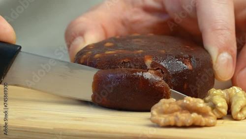 Close up of hands cut fresh apple pastille with walnuts on wooden cutting board. Apple cheese. Lithuanian cuisine