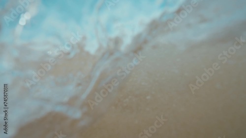 Small wave on white sand beach splashes over the camera in slow motion