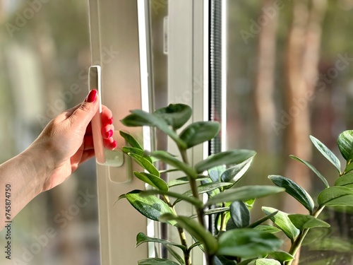 Person holding window handle in hand at open pvc frame for room airing close side view