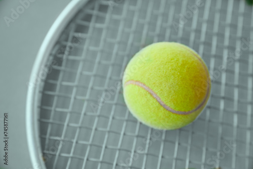 A yellow tennis ball lies on a tennis racket on a gray background.