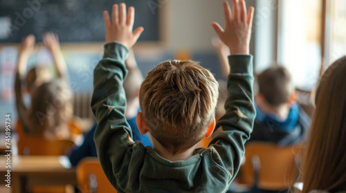 Elementary age student boy raised hands up in class. Volunteering and participating classroom concept.