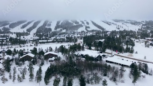 Ski resort town of Lindvallen in Sweden, in front of ski slopes with rotating ski lifts, many skiers and snowboarders going downhill from the snow covered mountain covered with pine forest photo