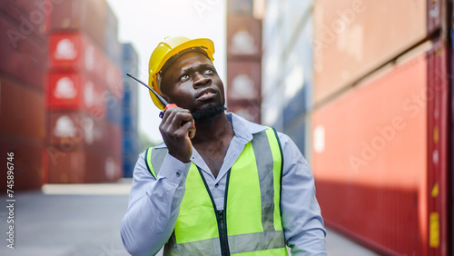 African american container male worker or dock foreman standing at warehouse logistic in Cargo freight ship for import export in harbor and talking to his team or someone with radio communication