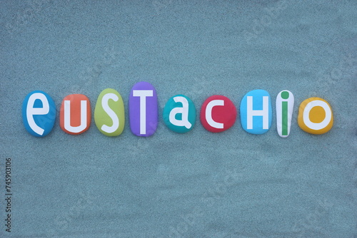 Celebration of Eustachio, Italian masculine first name composed with hand painted multi colored stone letters over green sand