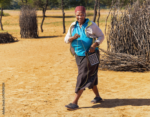 Canvastavla village old african woman using a solar panel with radio, to recharge phones and