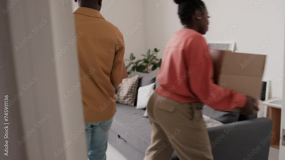 African American wife and husband bringing boxes into living room and unpacking belongings after moving in new flat African American wife and husband bringing boxes into living room and unpacking belongings after moving in new flat