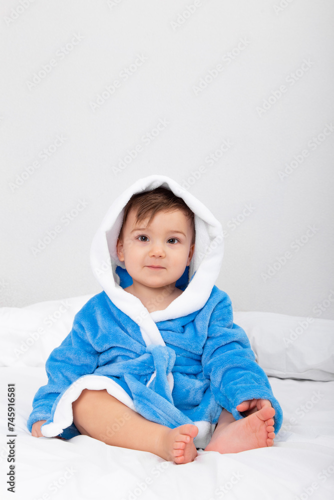 Baby in blue bathrobe, after bath, sitting on bed. Emotions, copy space. Baby in blue bathrobe, after bath, sitting on bed. Emotions, copy space.