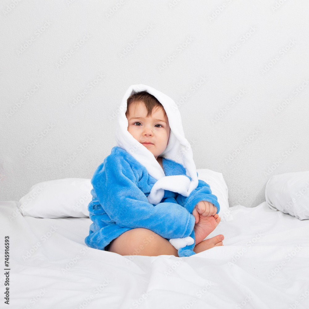 Baby in blue bathrobe, after bath, sitting on bed. Emotions, copy space. Baby in blue bathrobe, after bath, sitting on bed. Emotions, copy space.