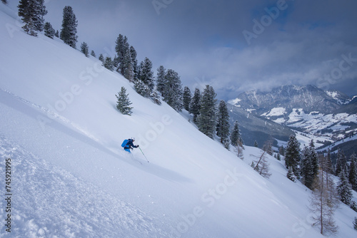 Skiing in deep powder snow in the mountains of Austria during winter, blue sky, in Hochfügen, mountain scenery in background. © Bastian Linder