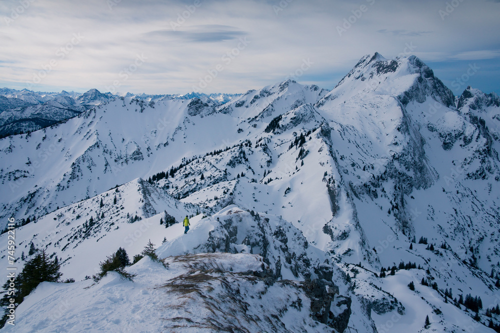 Man walking along snow-covered mountain ridge in the winter mountain panorama of Bavarian Alps of Ammergau, snowy mountain peaks in the background.