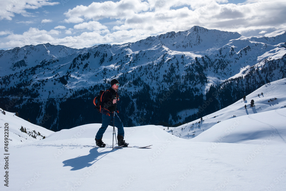 Man on mountain ski tour in the snow on sunny day, winter mountain panorama in background.