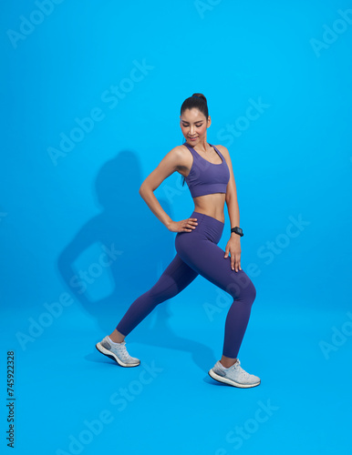 Asian Fitness sporty girl doing stretching workout. Full length shot of young woman warm up exercise isolated on blue background. Stretching and motivation