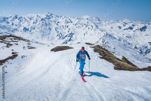 Man on mountain ski tour in the snow on sunny day, winter mountain panorama in background.