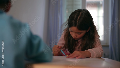 Little girl drawing on paper with coloring pen in bedroom by table. Concentrated child in leisure activity