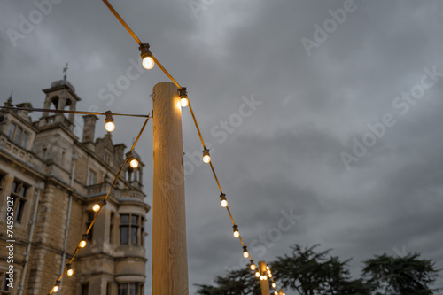 Strewn outdoor party lights seen attached to a wooden pole within the grounds of a Stately Home in the UK. The lights are in the large rear patio area of the stately home, for a public festival.